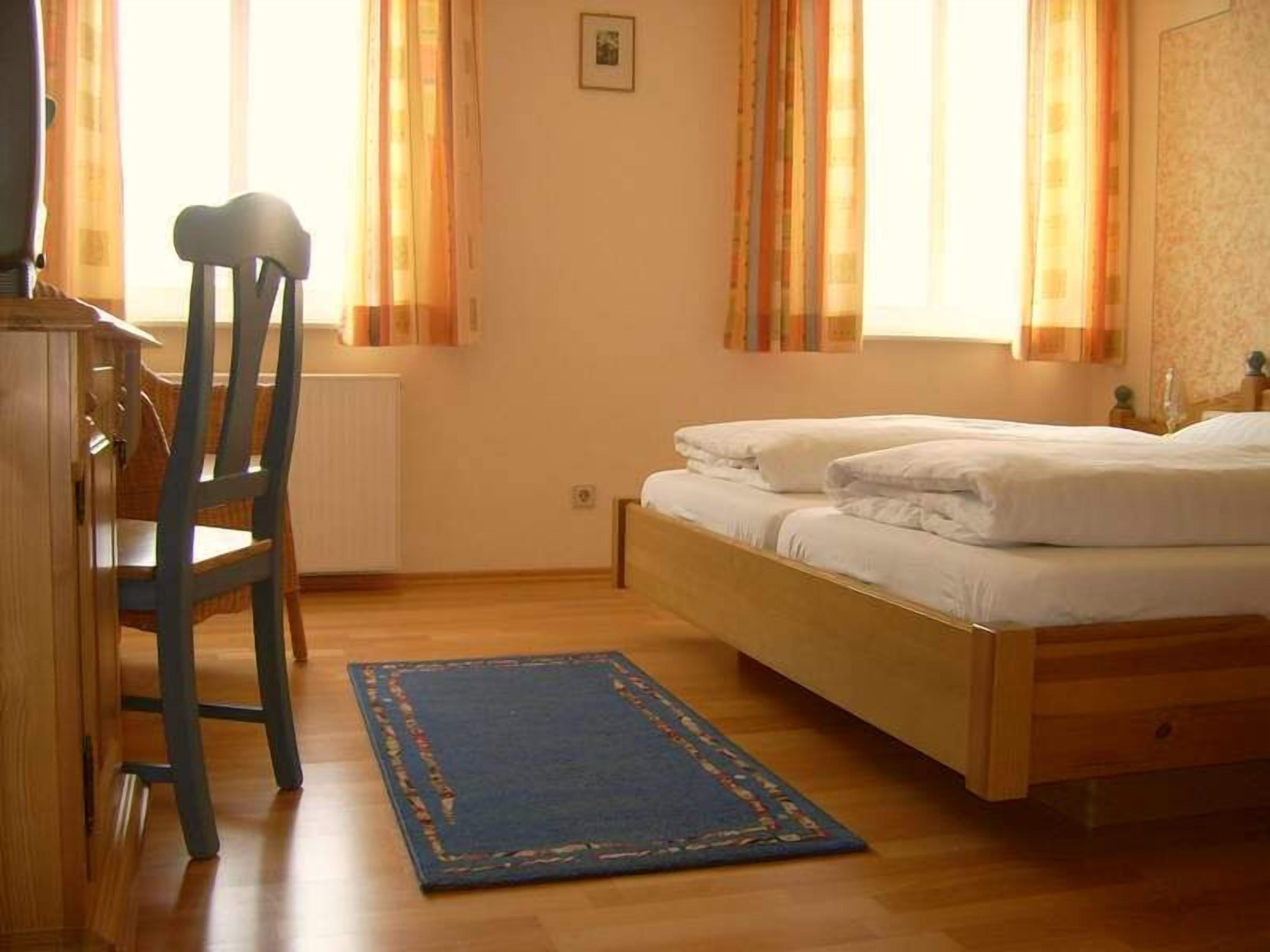 A bedroom with a wooden bed, a blue rug, a wooden chair, and a radiator.