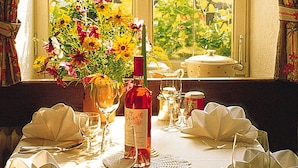 Mesa de comedor preparada para cuatro personas, con una botella de vino, copas y un florero.
