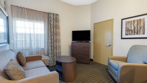 A hotel room with a sofa, a chair, a TV, a small table, and a door.