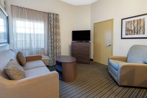 A hotel room with a sofa, a chair, a TV, a small table, and a door. - Candlewood Suites West Springfield by IHG (West Springfield)