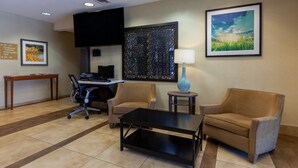 A hotel lobby with a reception desk, two sofas, a coffee table, a TV, and artwork on the walls.