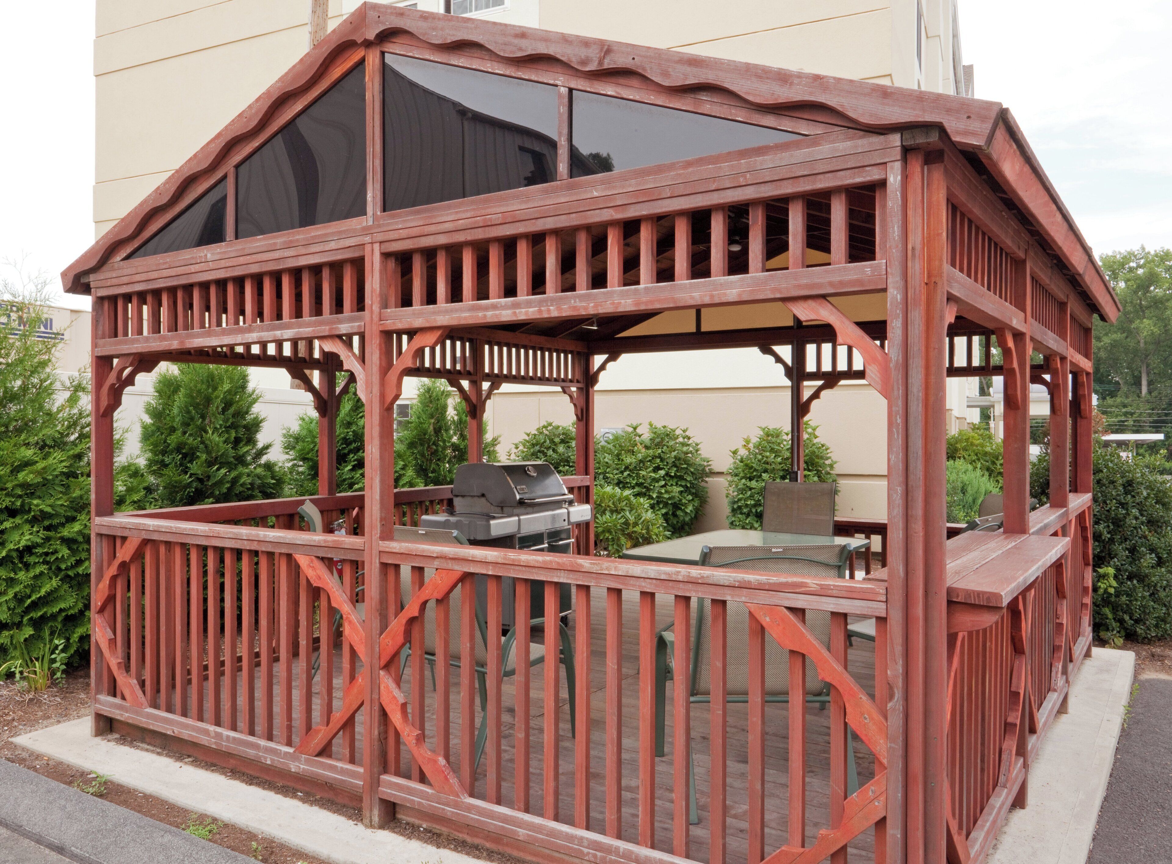 A wooden gazebo with a glass roof, a grill, and seating.