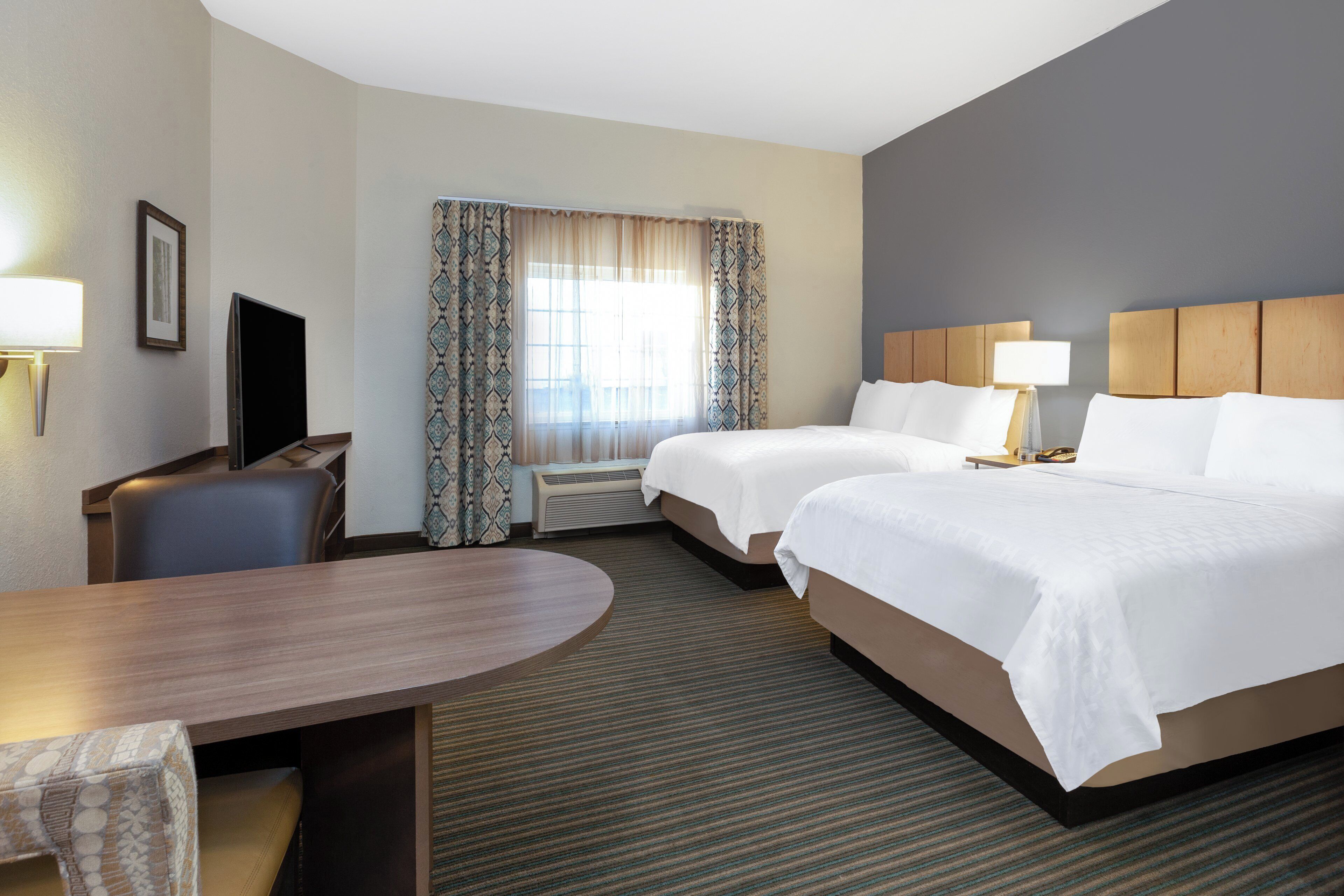 A hotel room with two beds, a desk, a chair, a TV, and a window with curtains.
