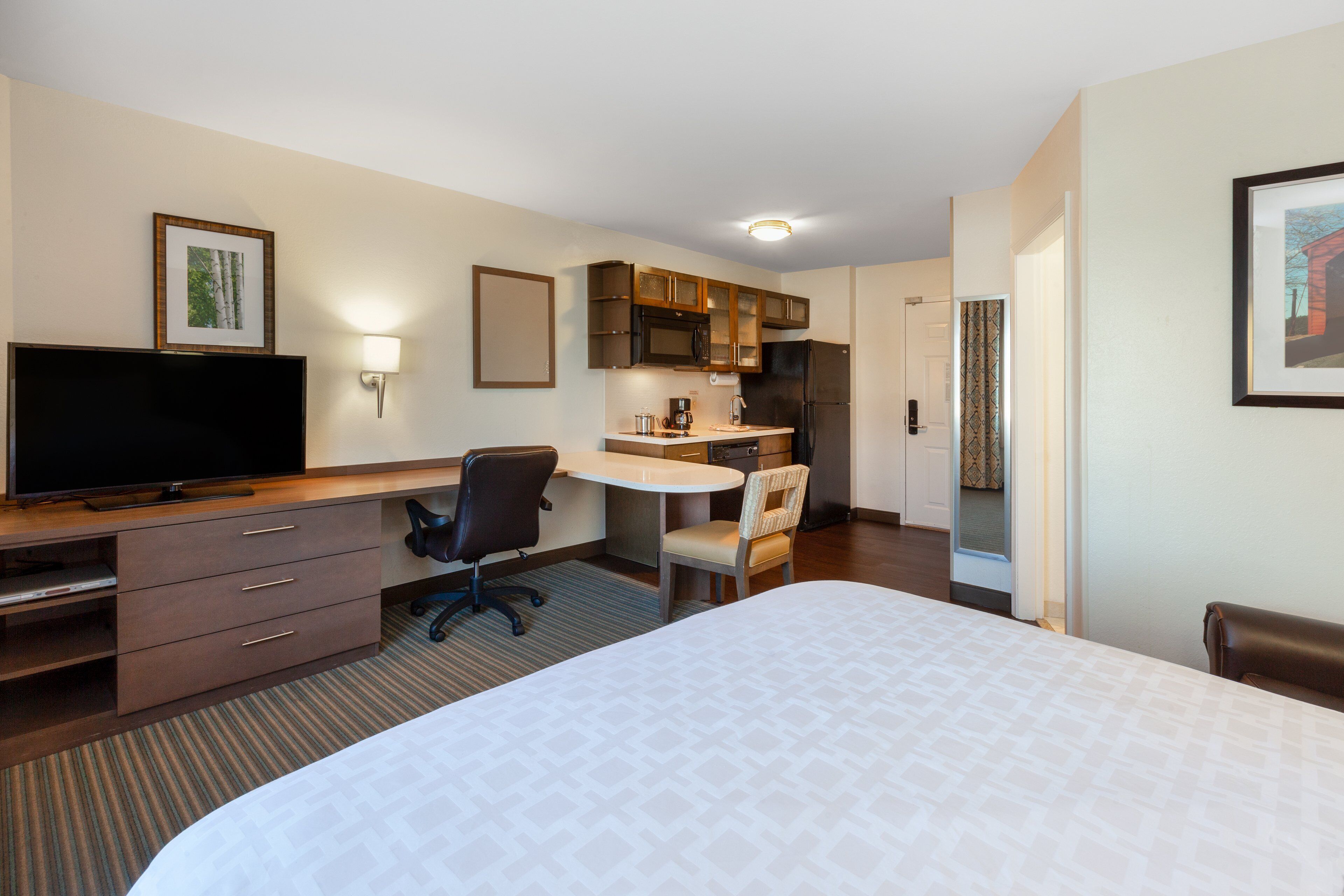 Habitación de hotel con cama, escritorio con silla, televisor, kitchenette y baño.