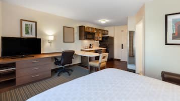 Habitación de hotel con cama, escritorio con silla, televisor, kitchenette y baño.