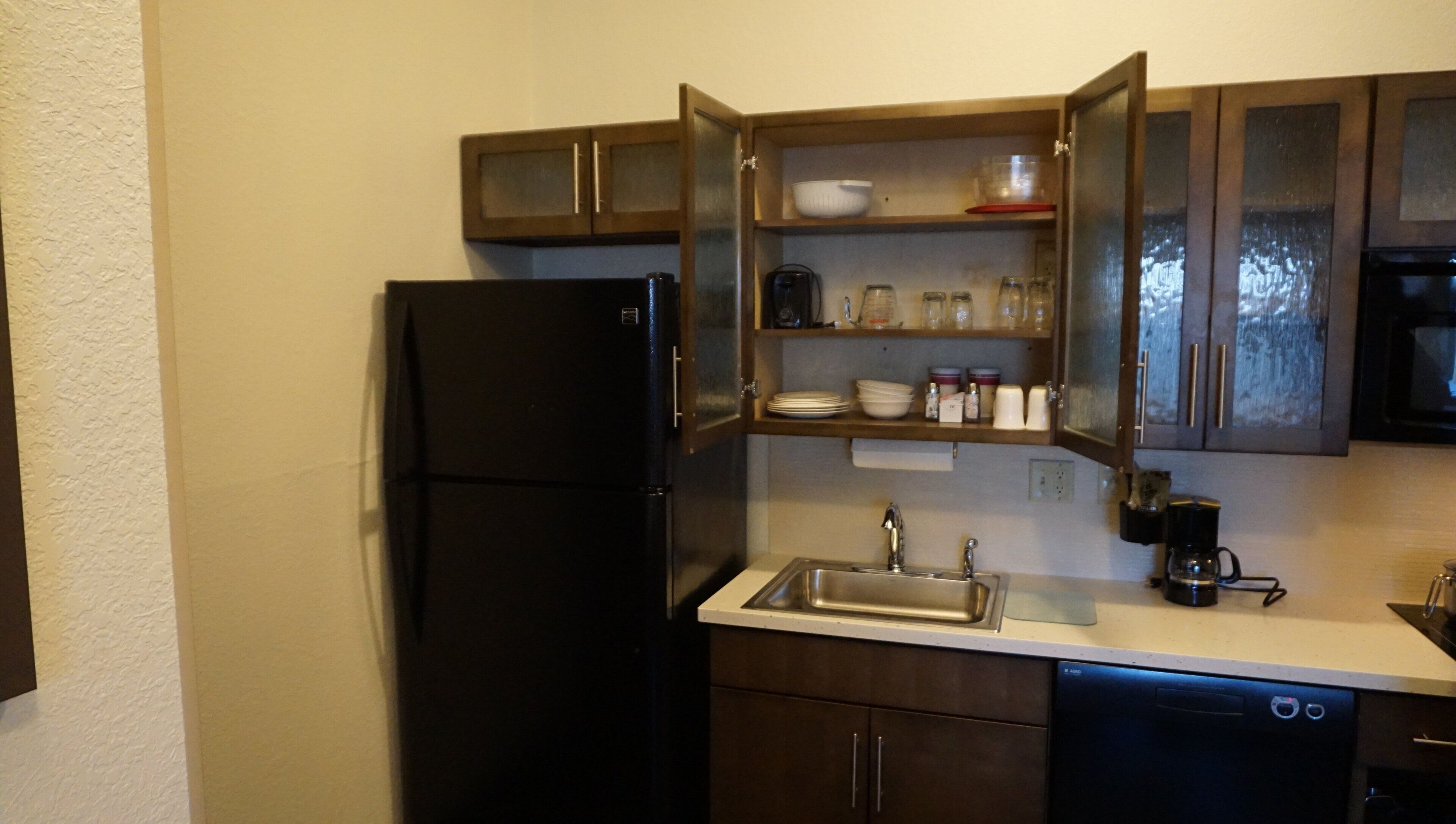 A compact kitchen with a black refrigerator, a sink, and wooden cabinets.