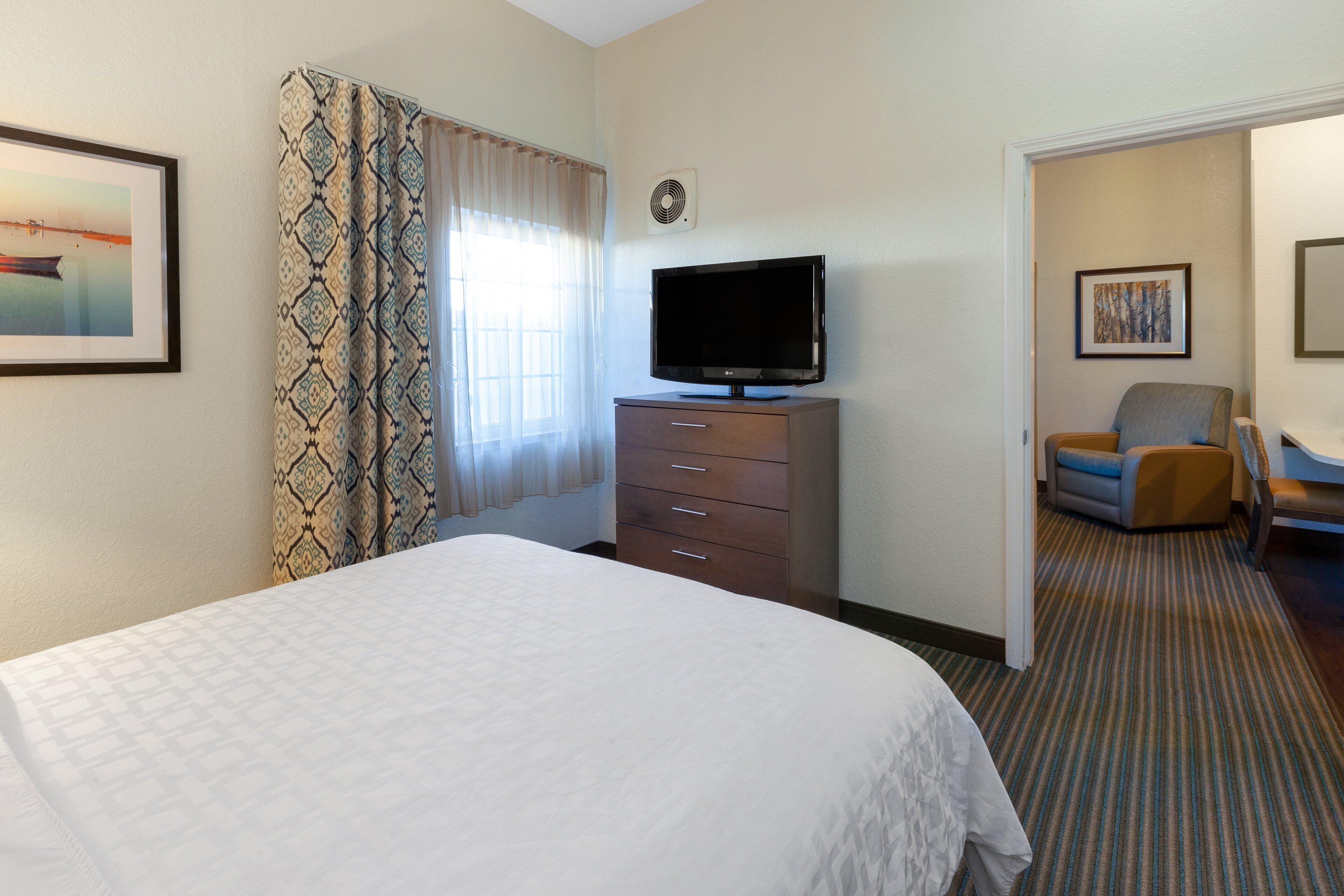 Une chambre d’hôtel avec un lit, un téléviseur posé sur une commode, une chaise et une porte donnant sur une autre pièce.