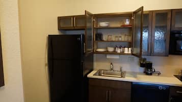 A compact kitchen with a black refrigerator, a stainless steel sink, wooden cabinets, and a dishwasher.