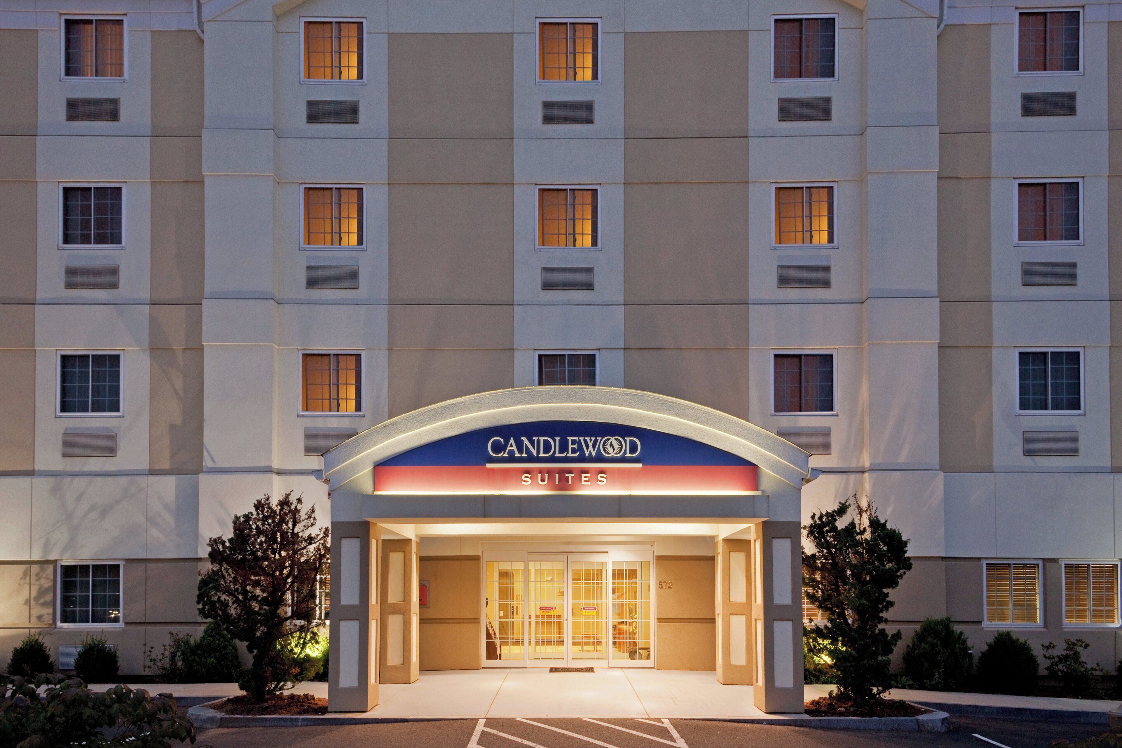 Een hotelentree met een bord waarop 'CANDLEWOOD SUITES' staat en een parkeerplaats ervoor.