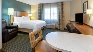 A hotel room with a bed, a desk, a chair, a TV, and a window with curtains.