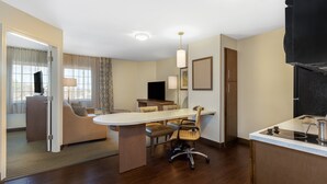A hotel room with a dining area, a sofa, a TV, and a kitchen area with a stove.
