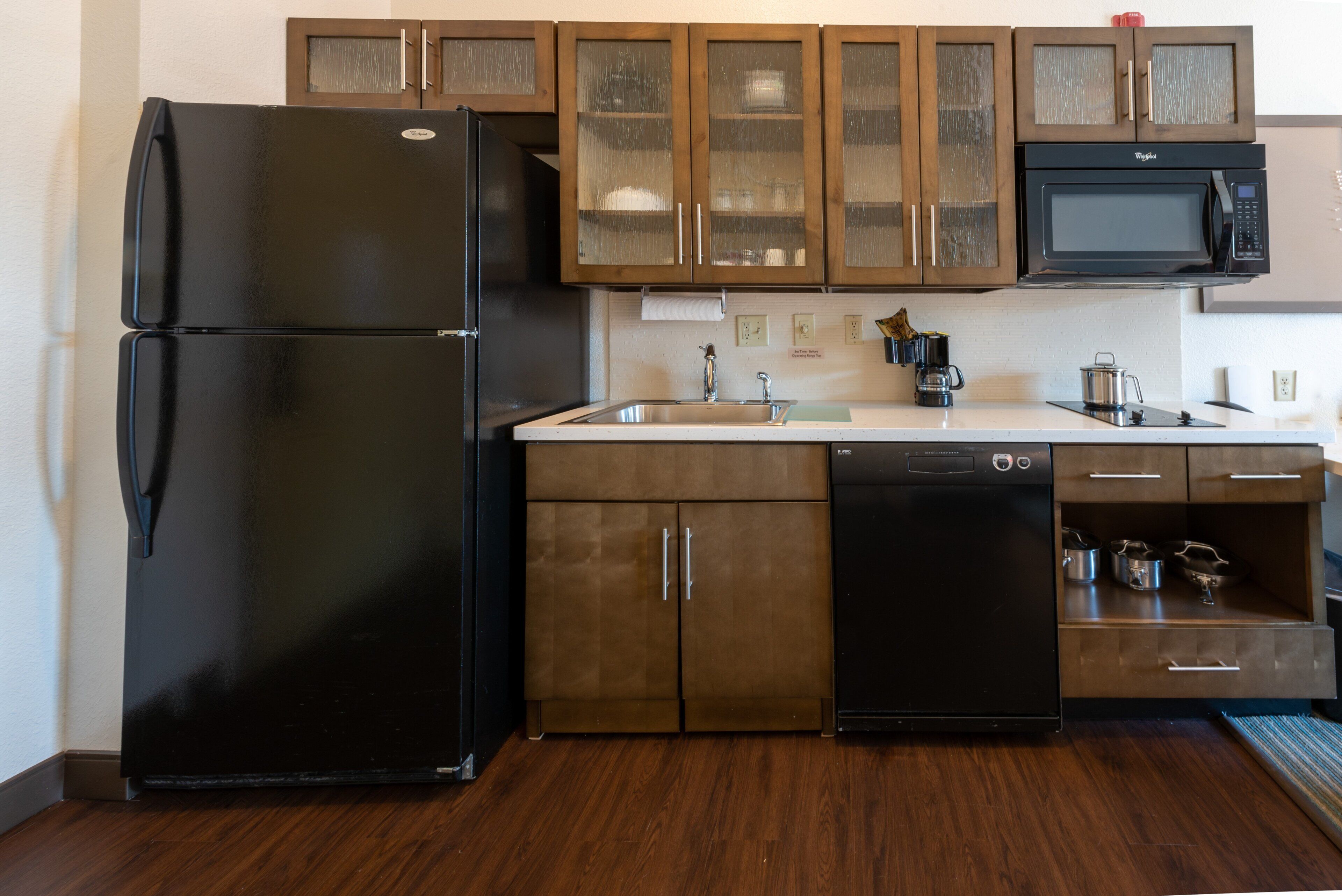 Una cucina con frigorifero nero, mobili in legno, forno a microonde ed elettrodomestici inclusi lavastoviglie.
