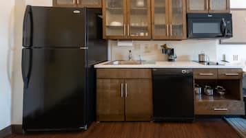 Una cucina con frigorifero nero, mobili in legno, forno a microonde ed elettrodomestici inclusi lavastoviglie.