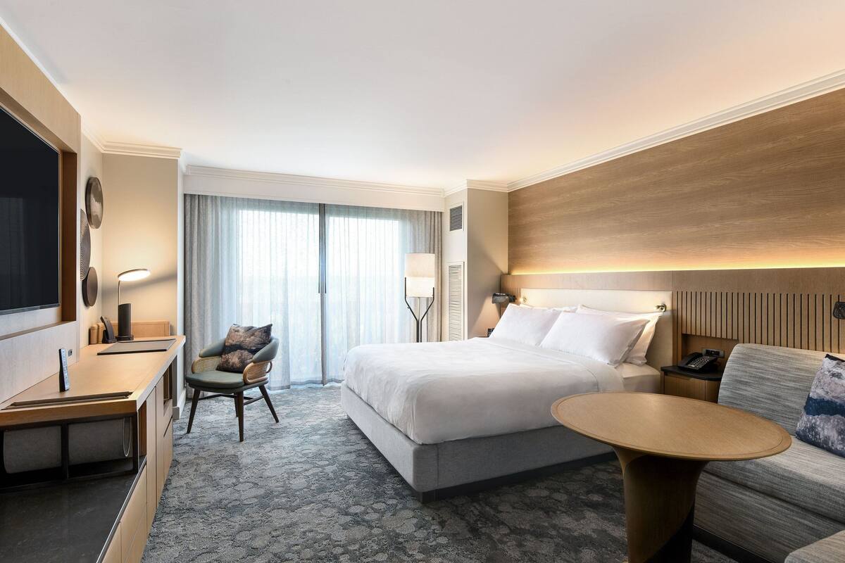 A hotel room with a bed, a desk, a chair, a sofa, and a TV.