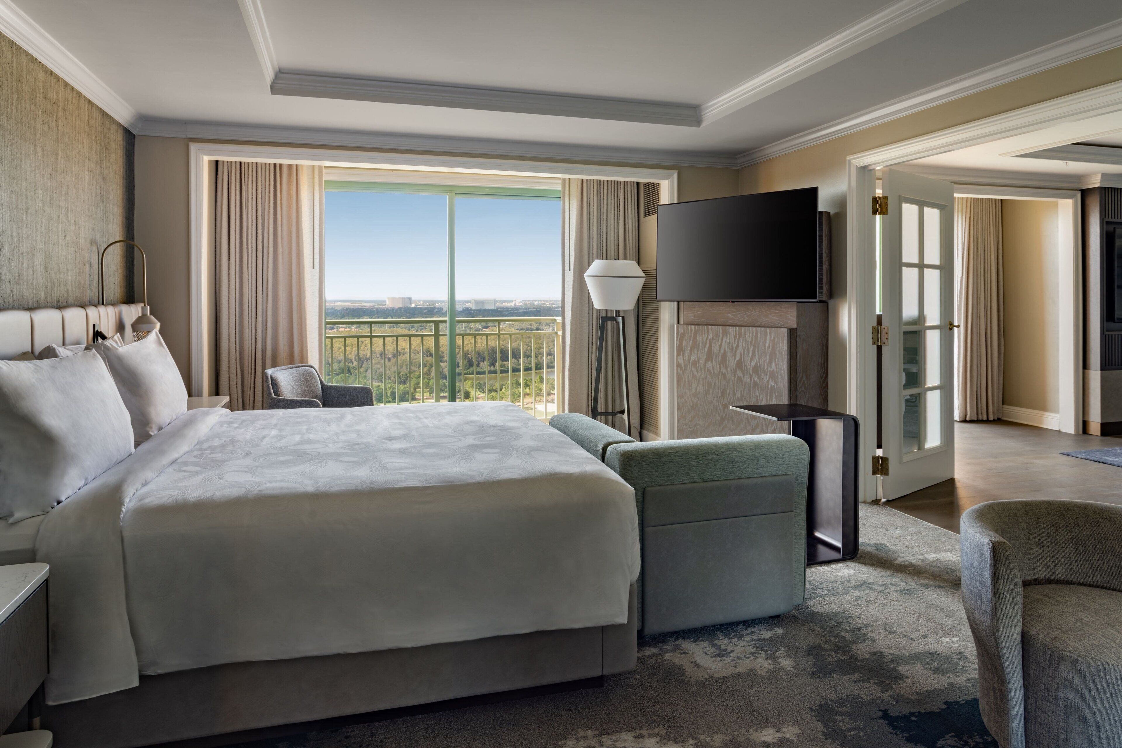 A hotel room with a large bed, a flat-screen TV, a sofa, and a view of the city.
