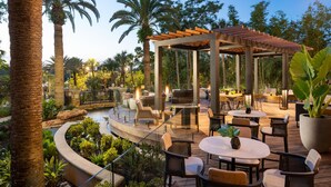 Un espace extérieur aménagé en terrasse, avec des tables et des chaises en bois, une pergola et un petit élément décoratif aquatique.