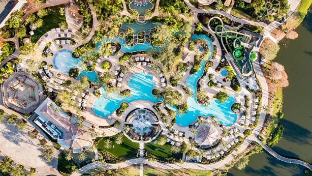 Une vue aérienne d’un complexe hôtelier doté de plusieurs piscines, de jardins aménagés et d’un pont reliant les différentes zones.