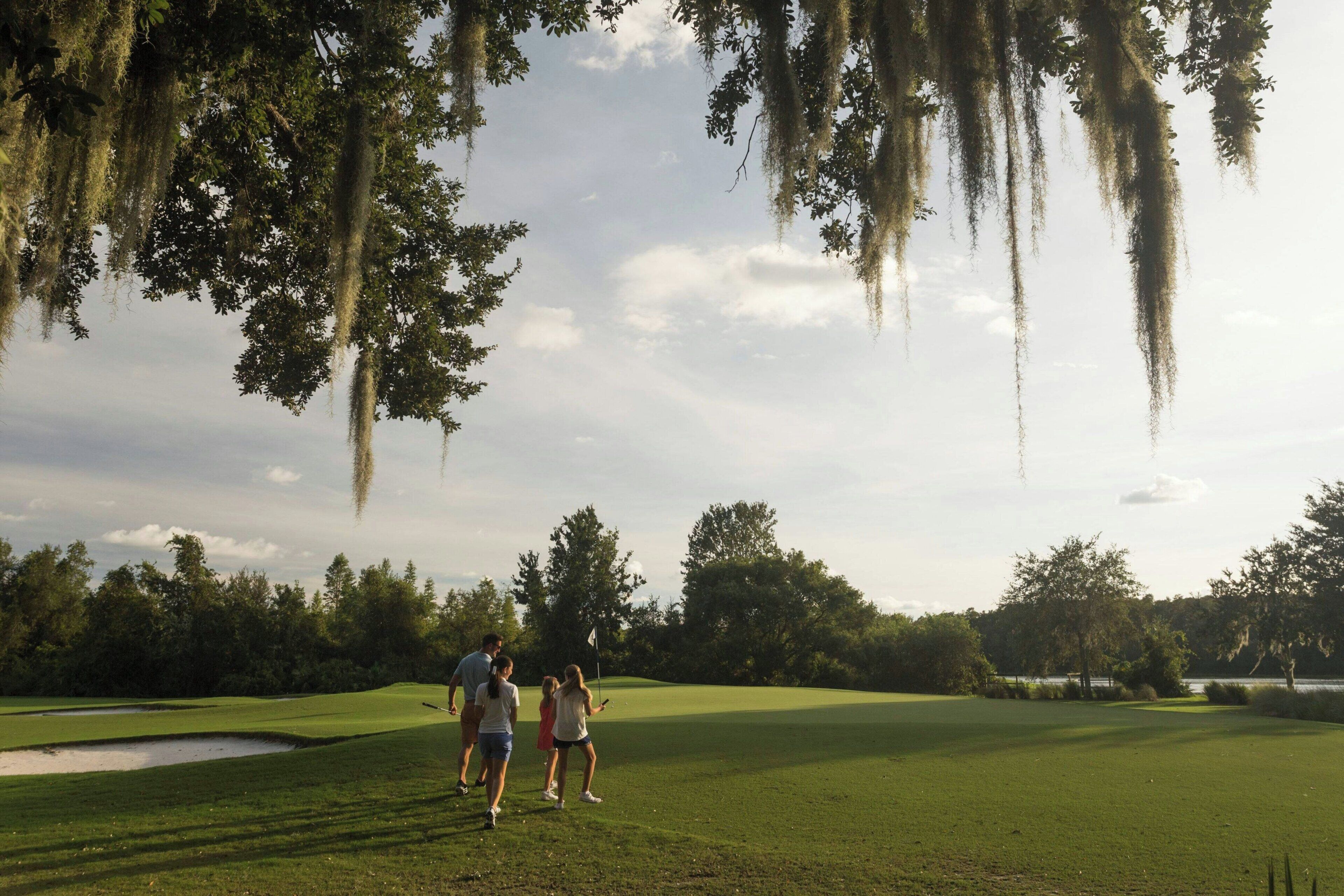 Un terrain de golf avec un mât de drapeau, des arbres et une étendue d’eau en arrière-plan.