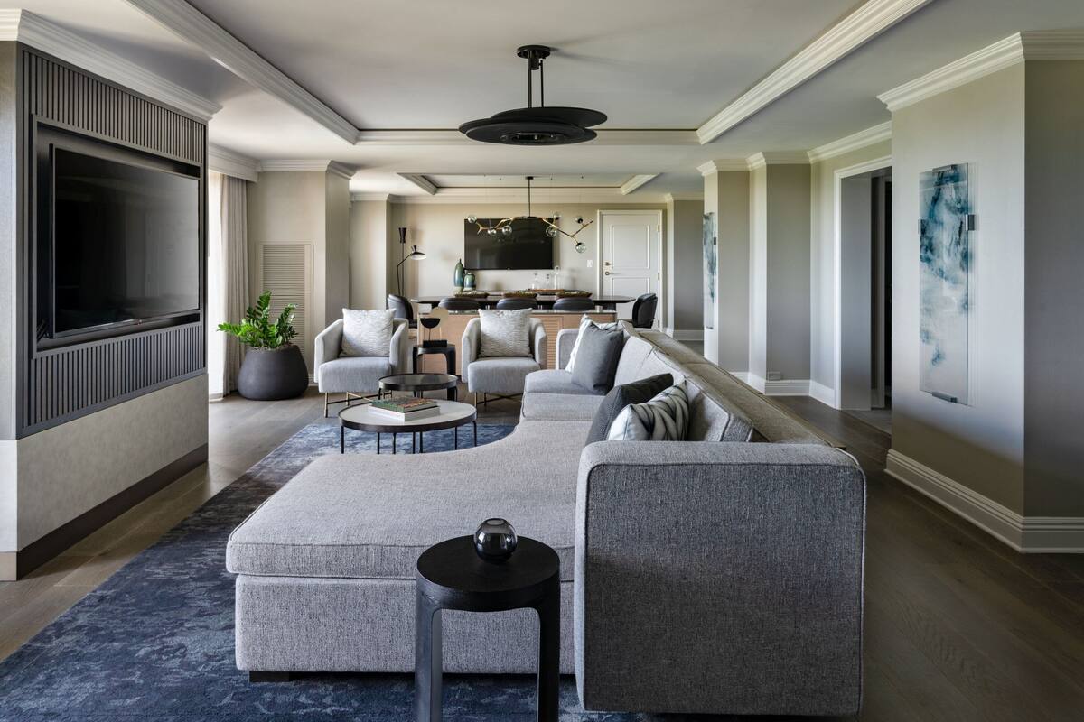 A modern living room with a sectional sofa, a flat-screen TV, and a dining area with a kitchen in the background.