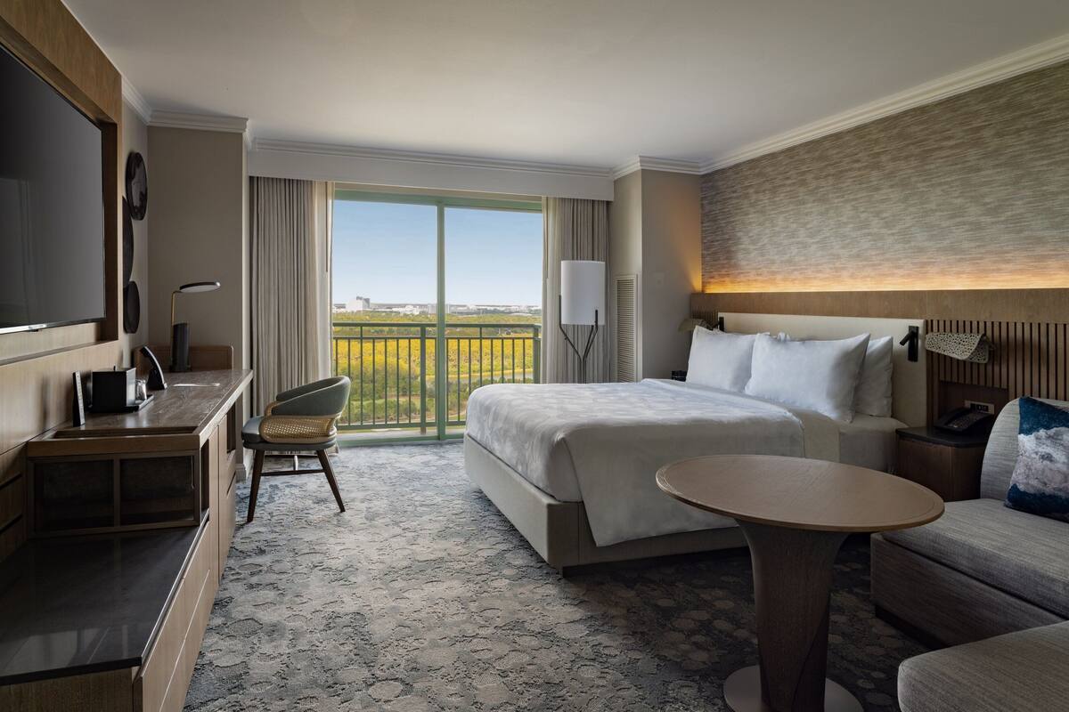 A hotel room with a large bed, a desk, a chair, a small round table, and a TV.