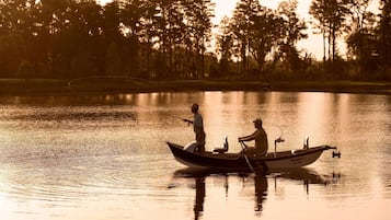Un bateau sur une étendue d’eau calme, avec deux personnes à bord, entouré d’arbres et avec un terrain de golf en arrière-plan.