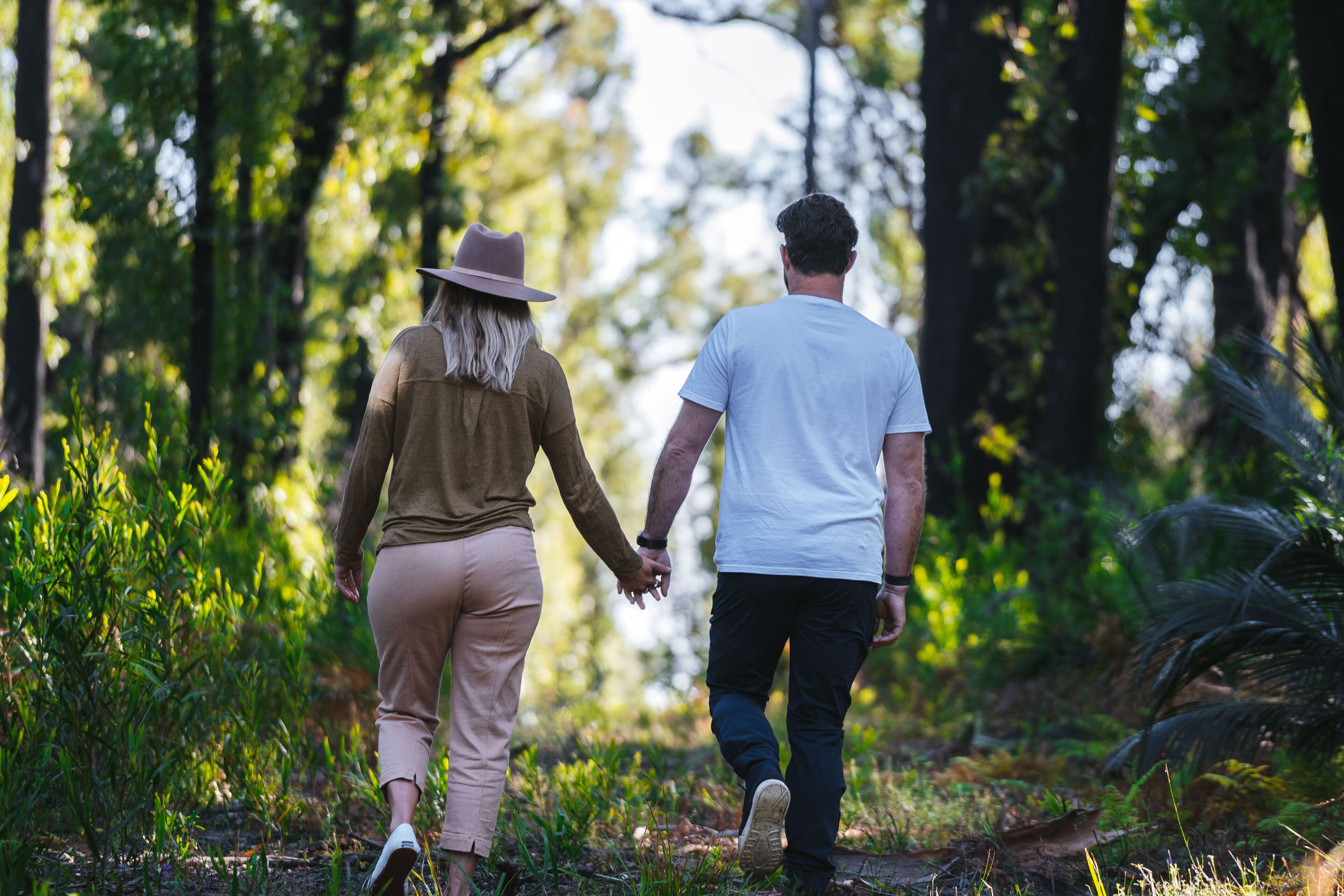 A couple walking hand in hand through a forested area.