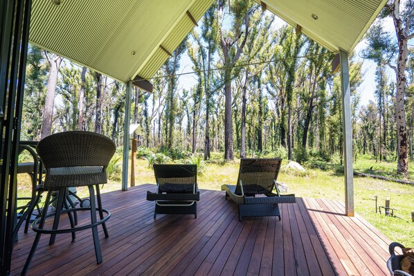 A wooden deck with wicker chairs and a table, overlooking a forested area.
