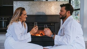 A couple seated in front of a fireplace in a modern, well-lit room with a large window. - The Bower at Broulee (Broulee)
