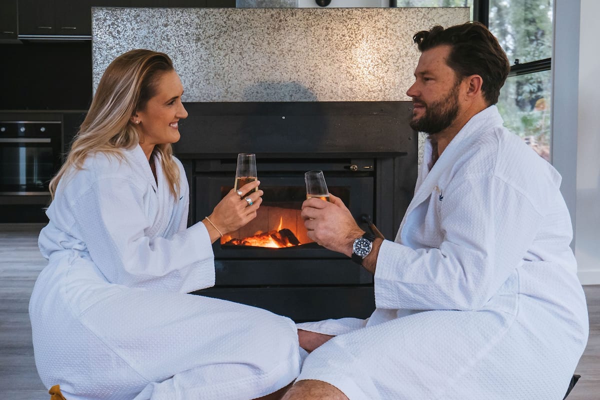 A couple seated in front of a fireplace in a modern, well-lit room with a large window.