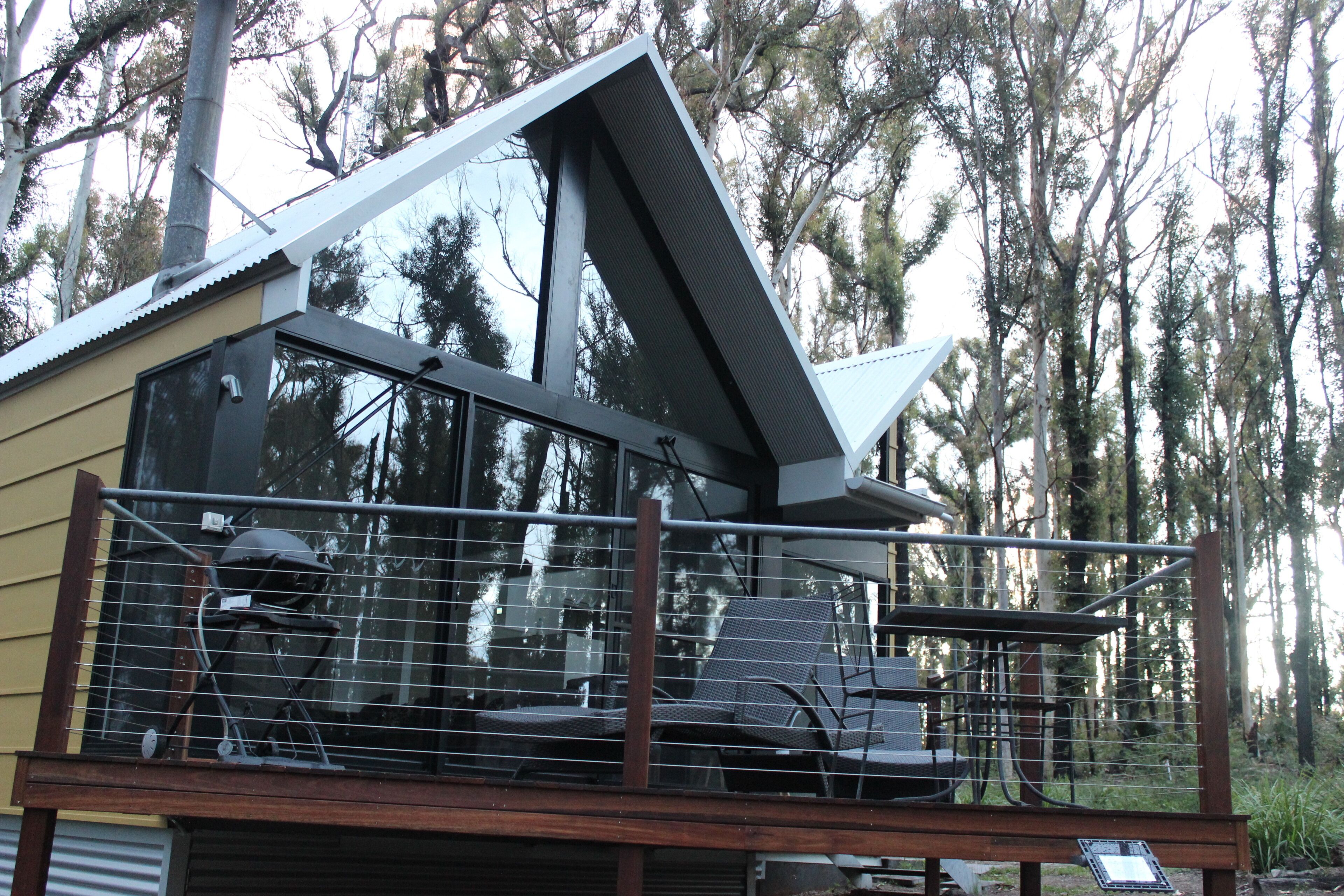 A modern building with a balcony, large windows, and a view of trees.