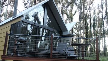A modern building with a balcony, large windows, and a view of trees.
