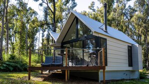 A modern cabin with a large deck, surrounded by trees. - The Bower at Broulee (Broulee)