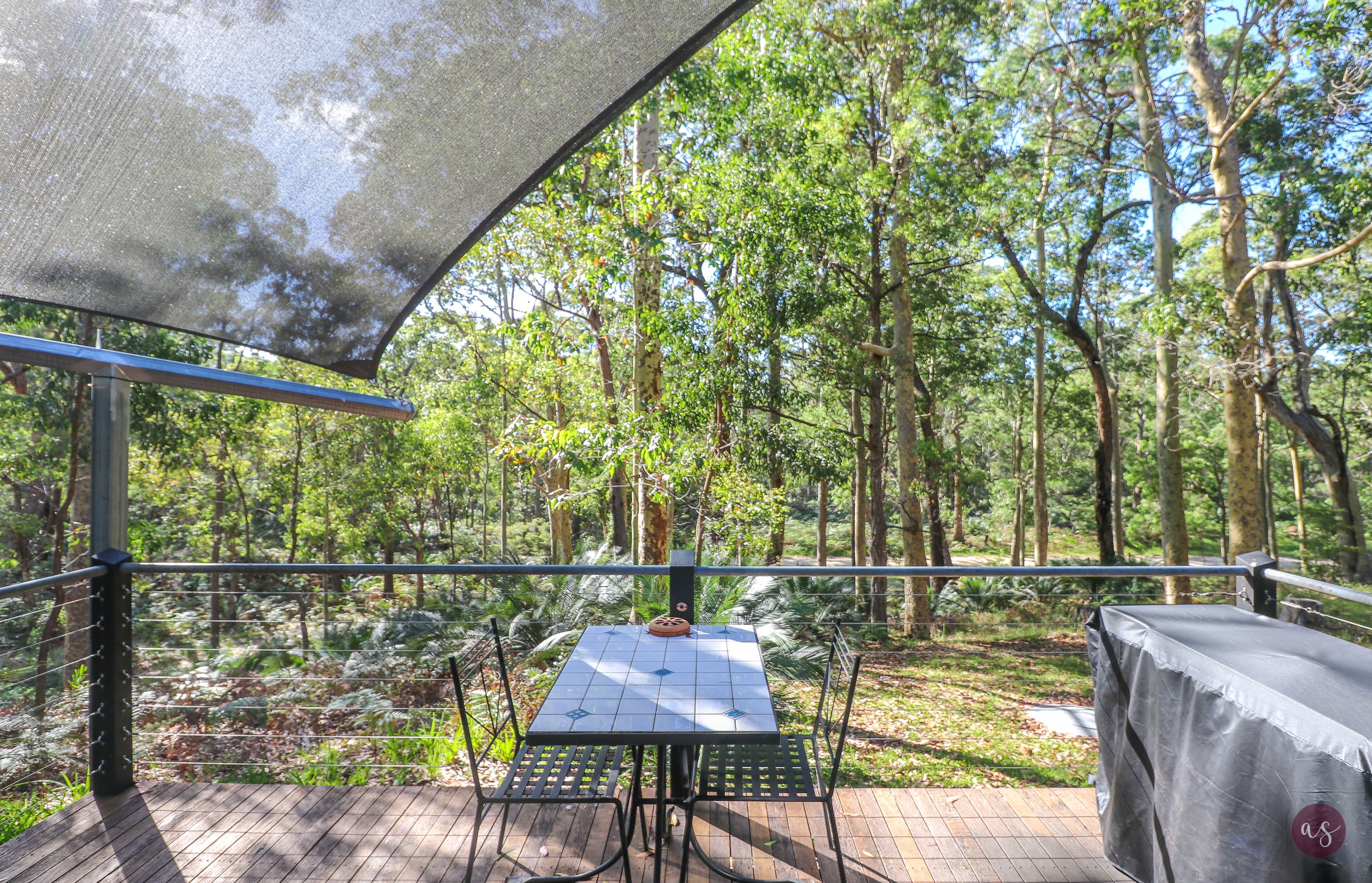 A covered outdoor area with a table and chairs, surrounded by trees.