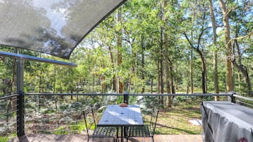 A covered outdoor area with a table and chairs, surrounded by trees.