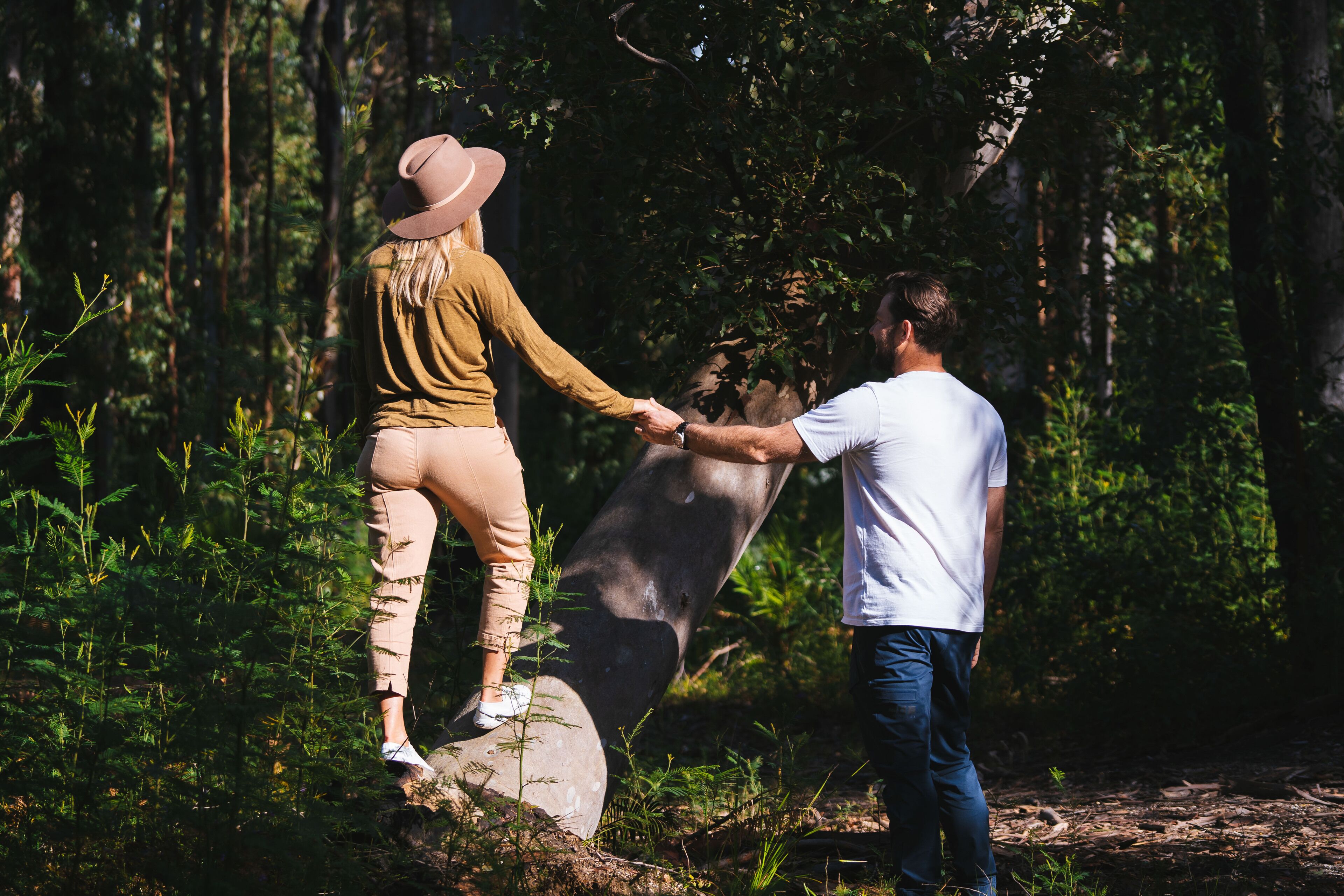 Dos personas tomadas de la mano sobre una roca en un área boscosa.