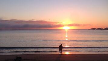 Eine Strandansicht, eine Person steht zum Sonnenuntergang hin.