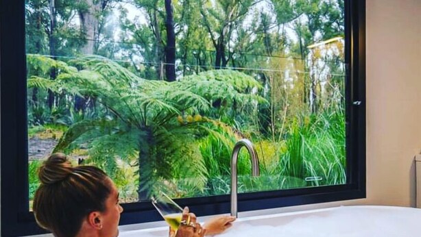 A person in a bathtub with a view of a lush garden through a large window. - The Bower at Broulee (Broulee)