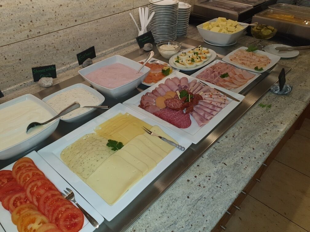 Un bufé con diversos alimentos, incluyendo tomates en rodajas, distintos tipos de queso y una variedad de carnes.