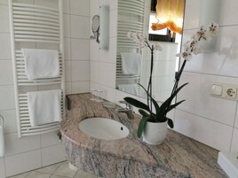 A bathroom with a granite sink, white tiles, a towel rack, a mirror, and an orchid plant.