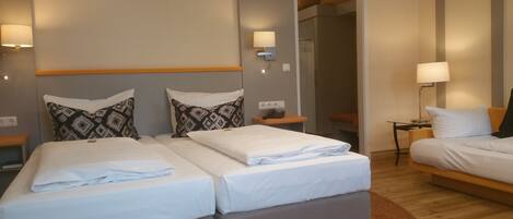 Une chambre d’hôtel avec deux lits, un plancher en bois et une salle de bain visible à travers une porte ouverte.