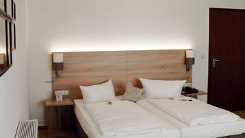 Habitación de hotel con una cama doble, una mesita de noche con lámpara, cabecera de madera y una puerta.