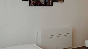Habitación de hotel con cama, aire acondicionado de pared y varias fotografías enmarcadas.