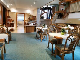 A hotel dining area with wooden furniture, a central island with dishes, and a staircase leading to an upper level.