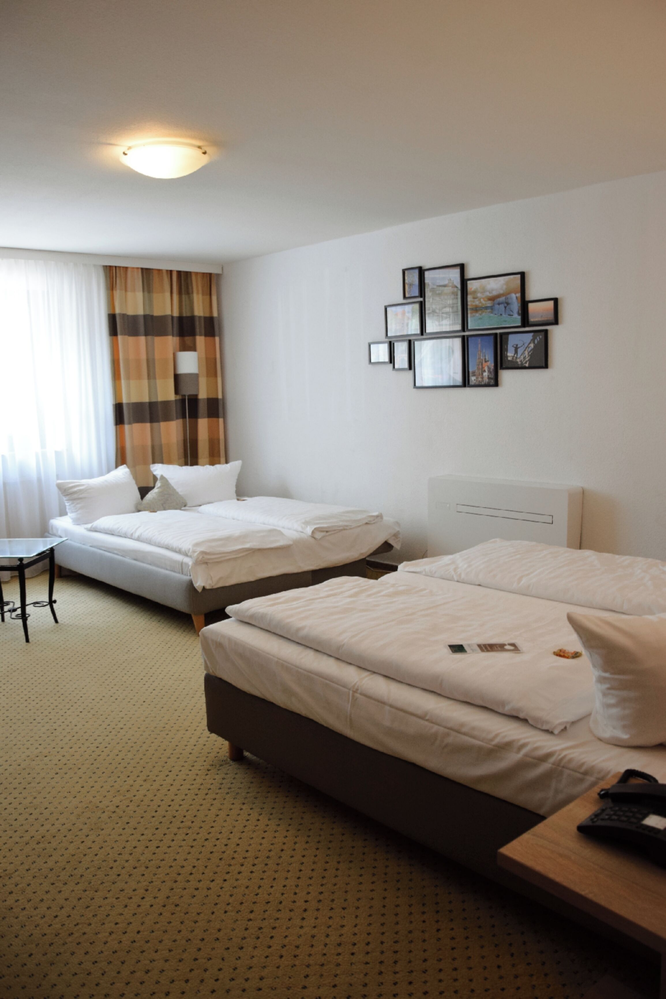 Habitación de hotel con dos camas, un escritorio y una pared decorada con cuadros.