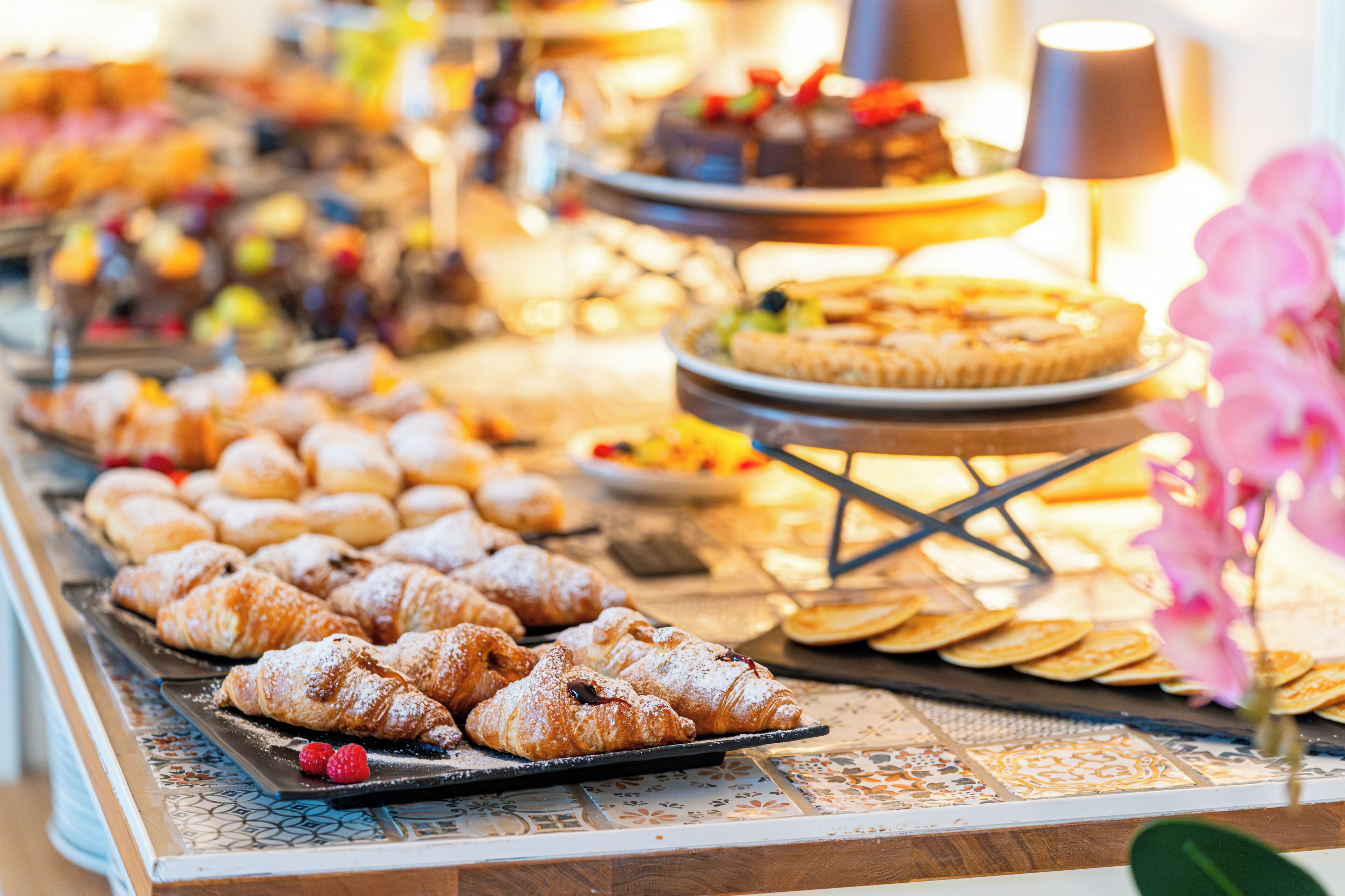 Un buffet con dolci, tra cui croissant e una torta, su un tavolo con una tovaglia fantasia.