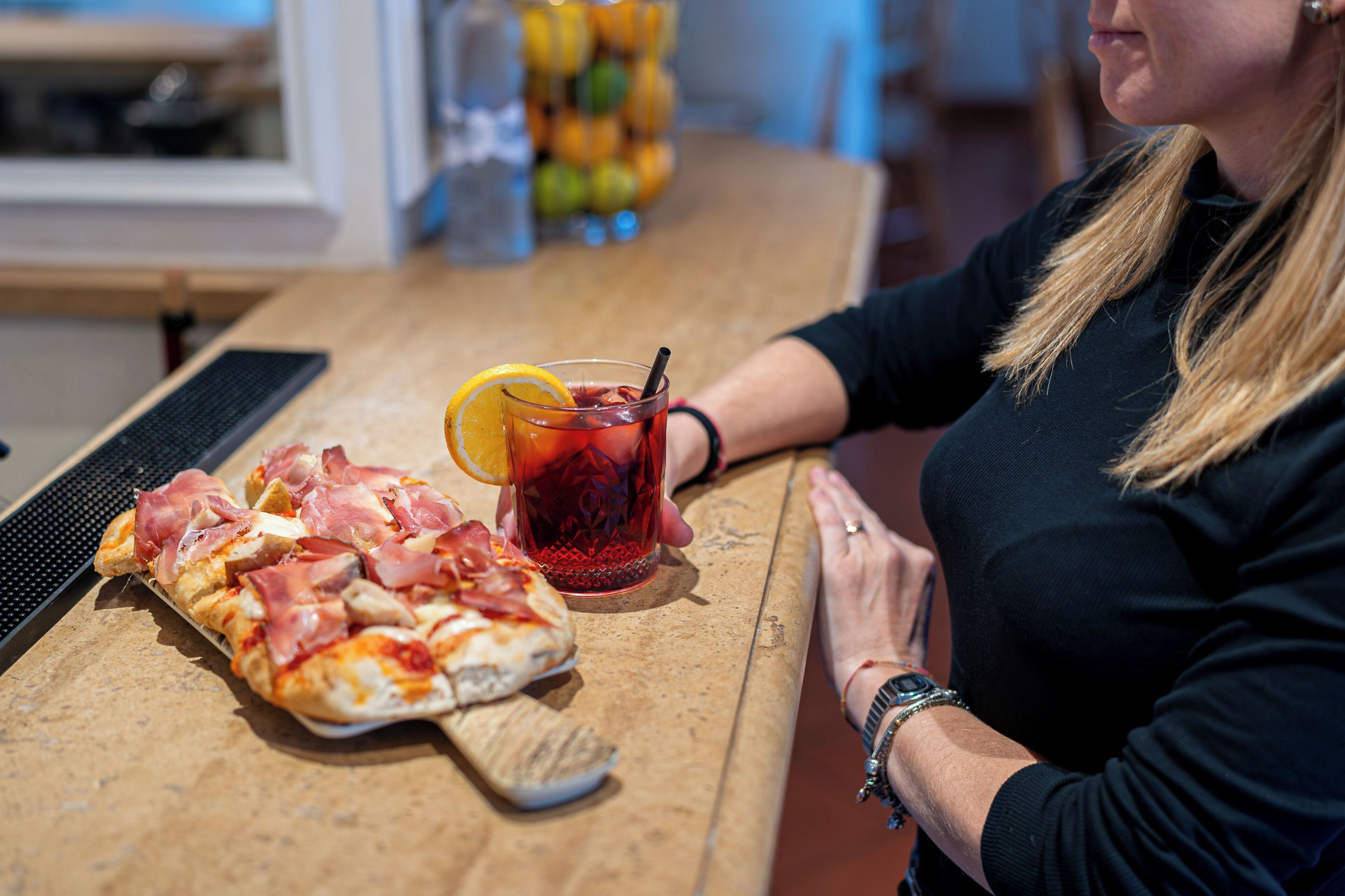 A person seated at a table with a pizza and a glass of iced tea.