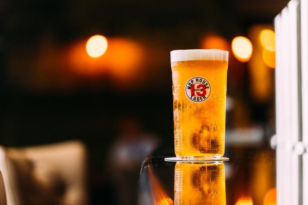 A glass of beer with a logo on the side, placed on a reflective surface.