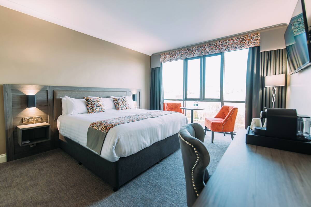 A hotel room with a bed, a desk, a chair, a nightstand, and a window with curtains.