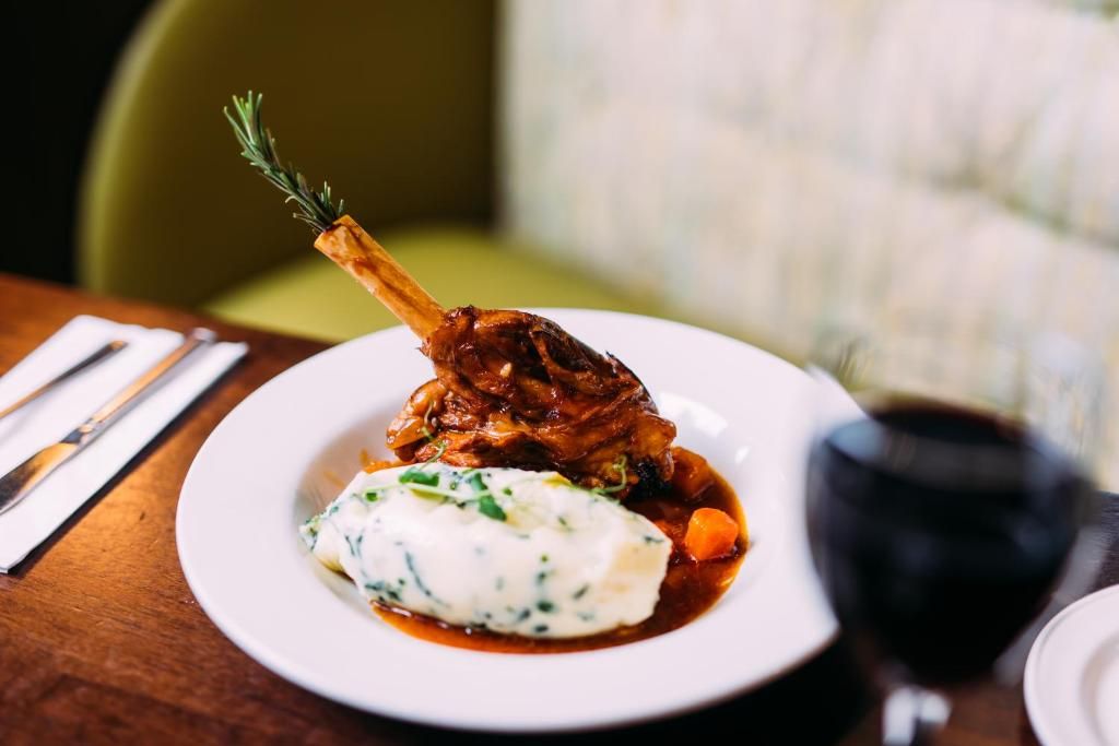 A plate of food with a lamb shank, mashed potatoes, and a side of vegetables.