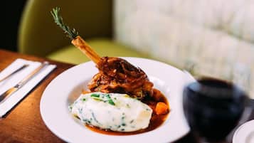 A plate of food with a lamb shank, mashed potatoes, and a side of vegetables.